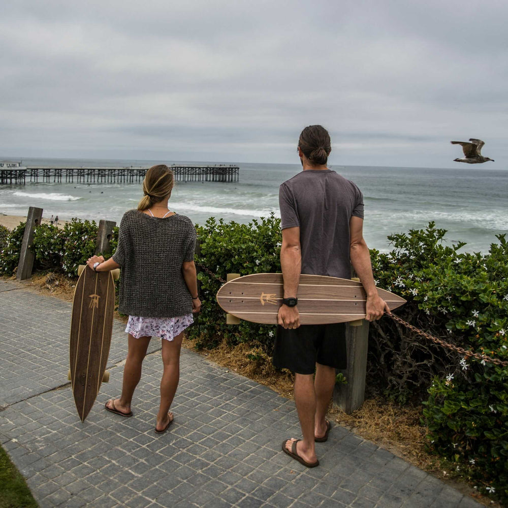 Man and woman holding Tower boardwalk cruiser skateboards while overlooking the ocean