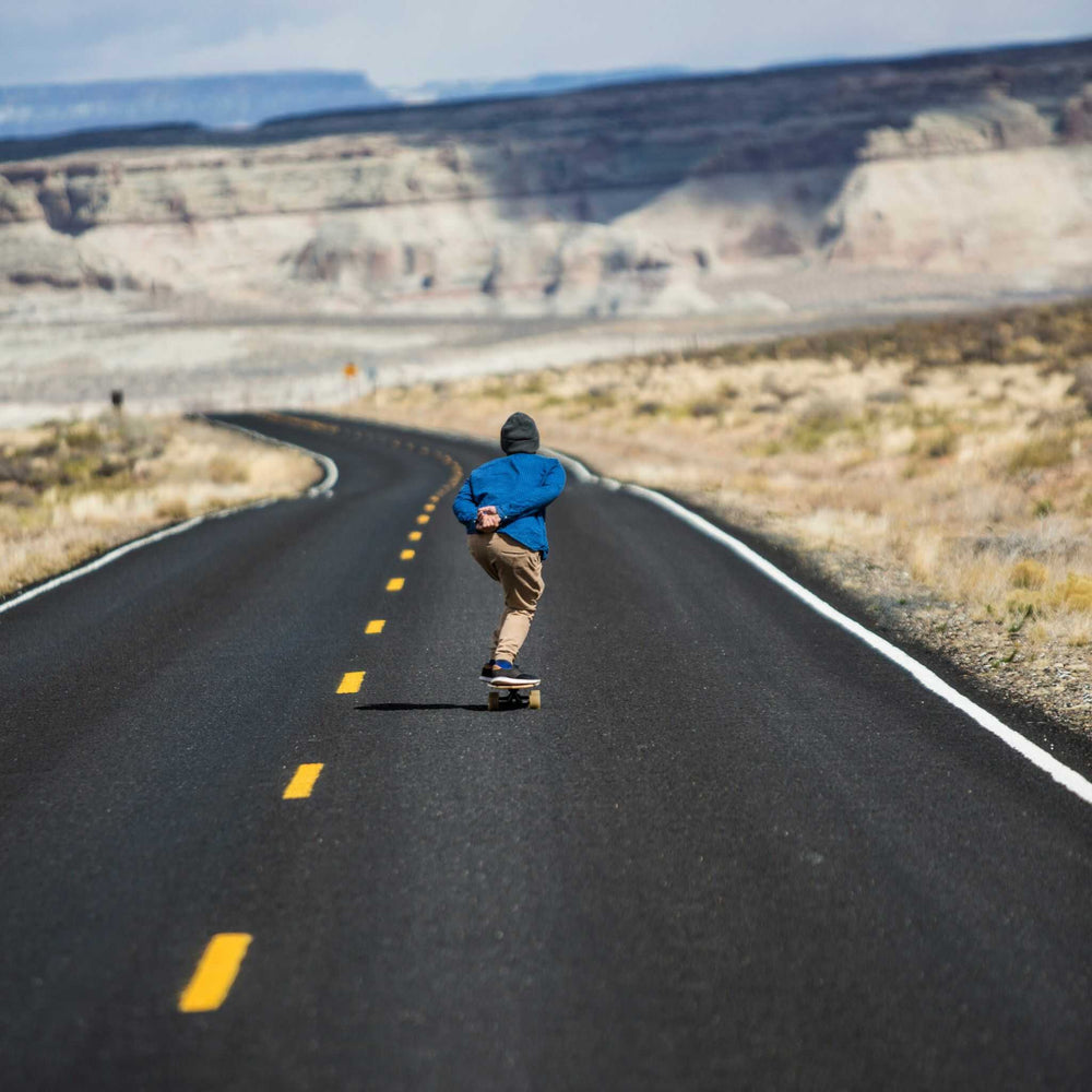 Man riding a Tower skateboard down an empty highway in the desert