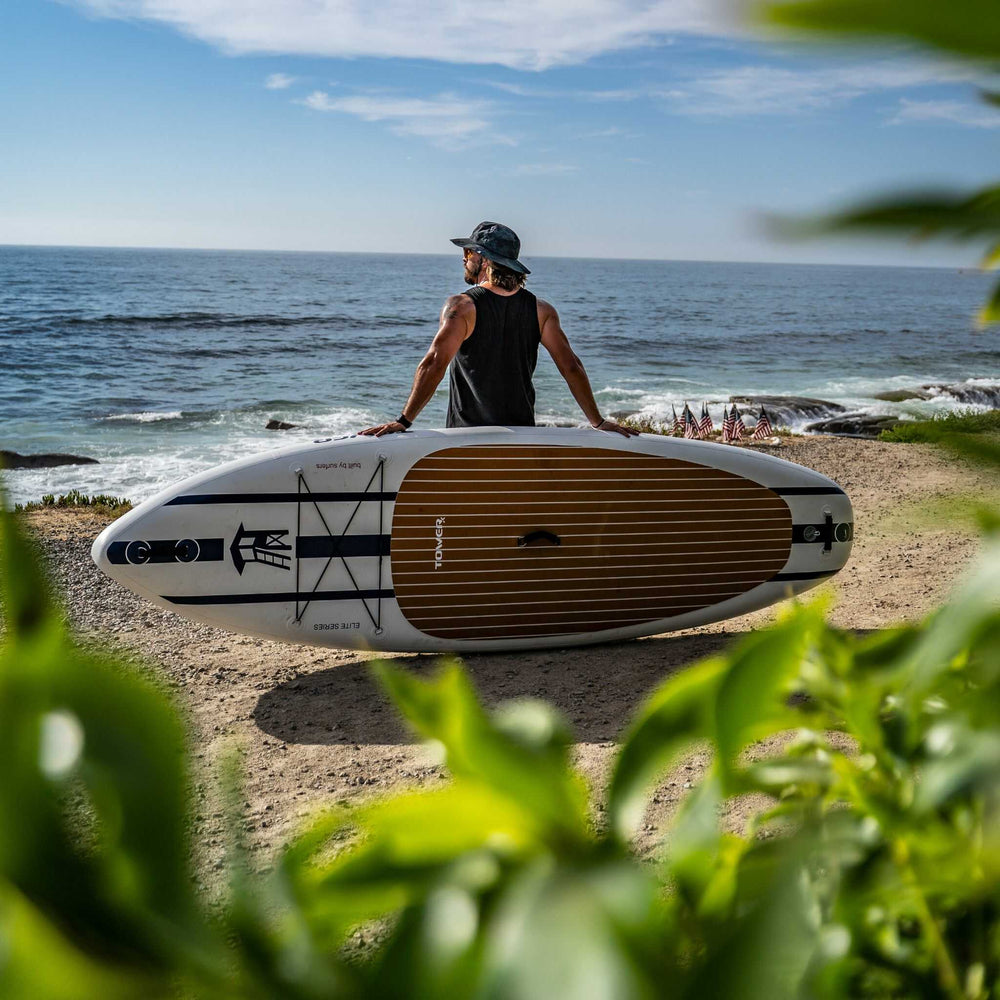 Man leaning against a Tower X-class board on a shoreline