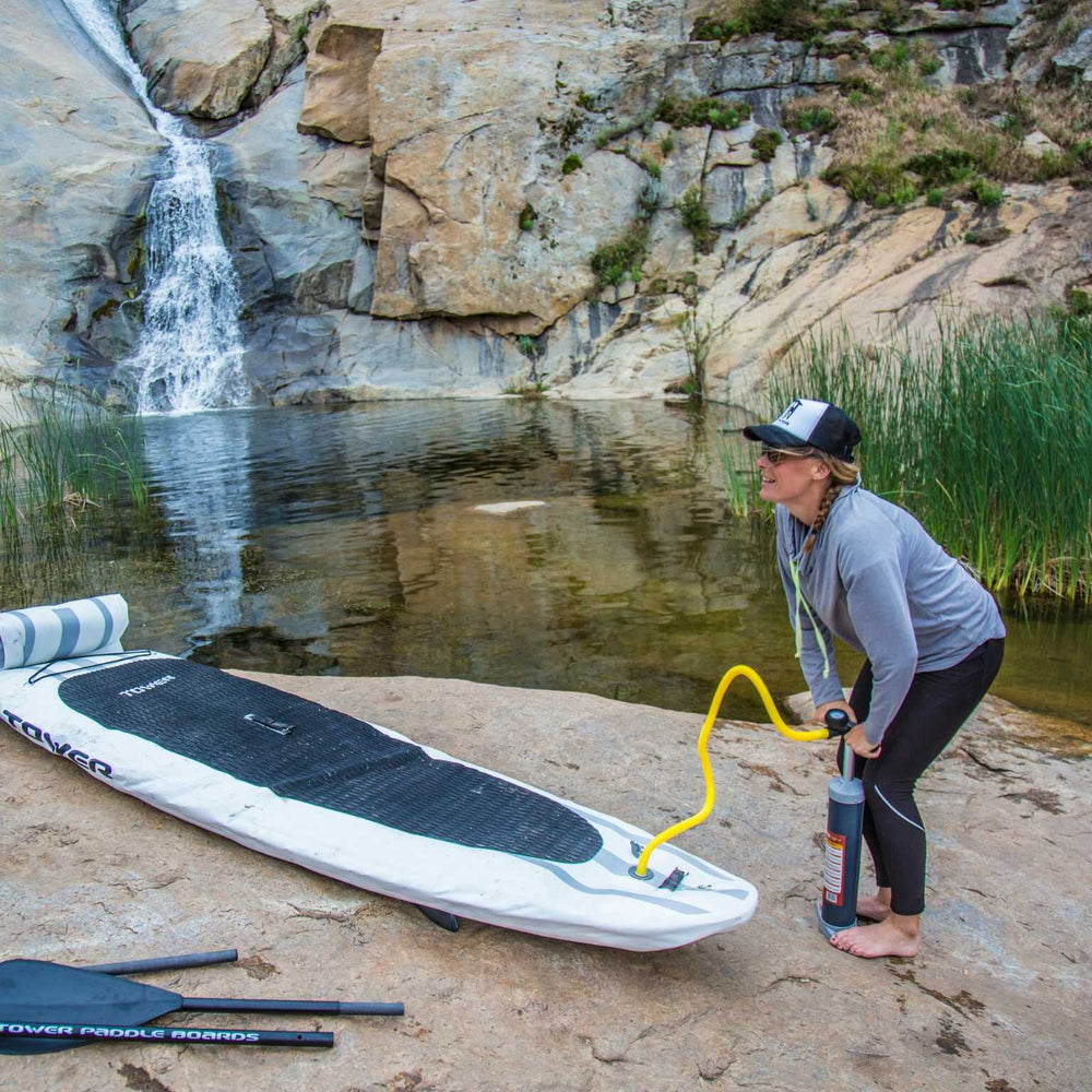 Woman inflating a Tower paddle board next to a pond and waterfall