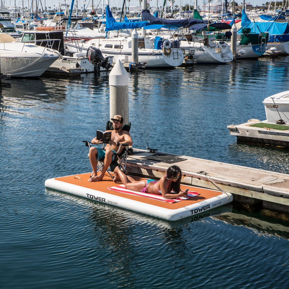 Man sitting in chair and woman laying down on a Tower swim step in the water