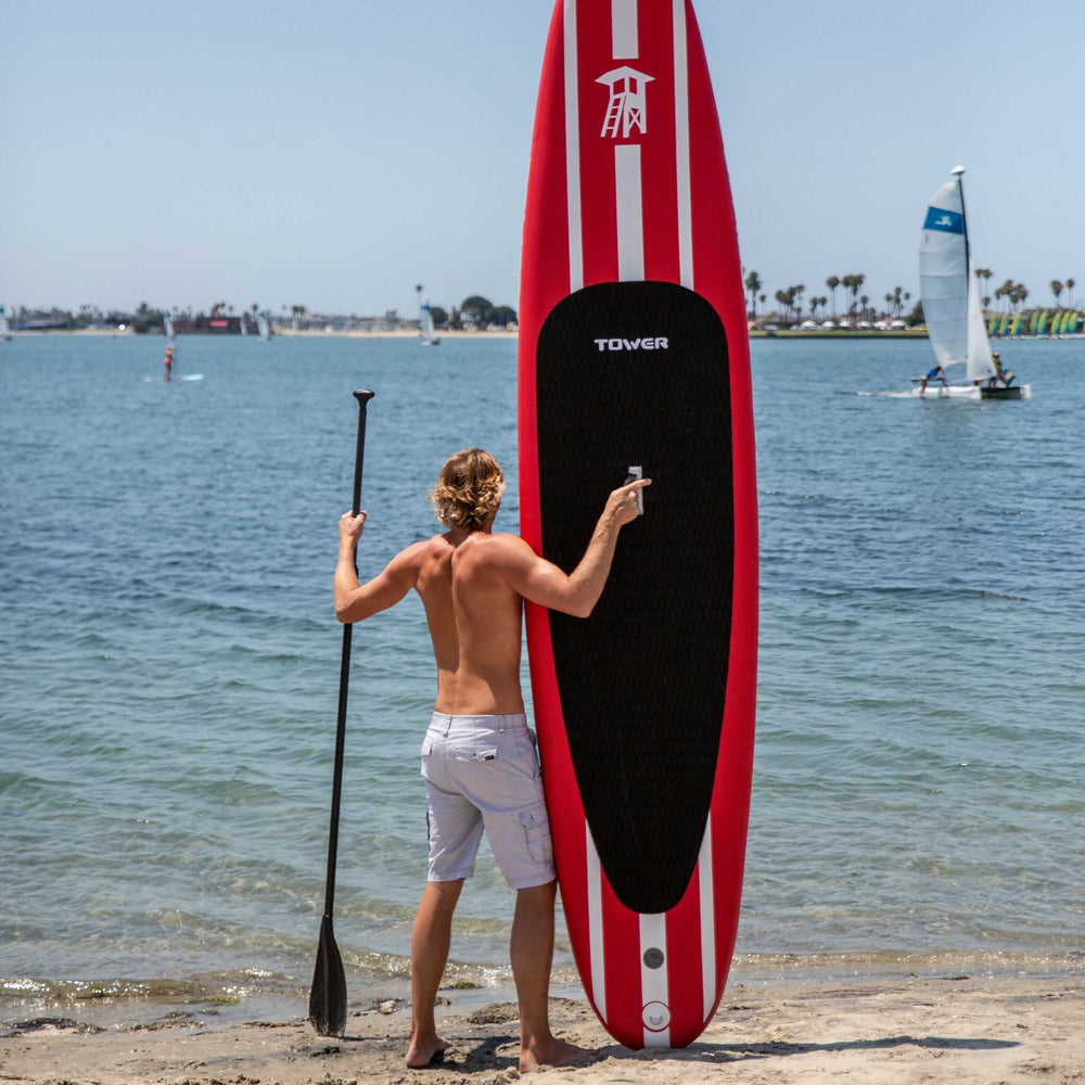 man standing with red Tower paddle board on shore