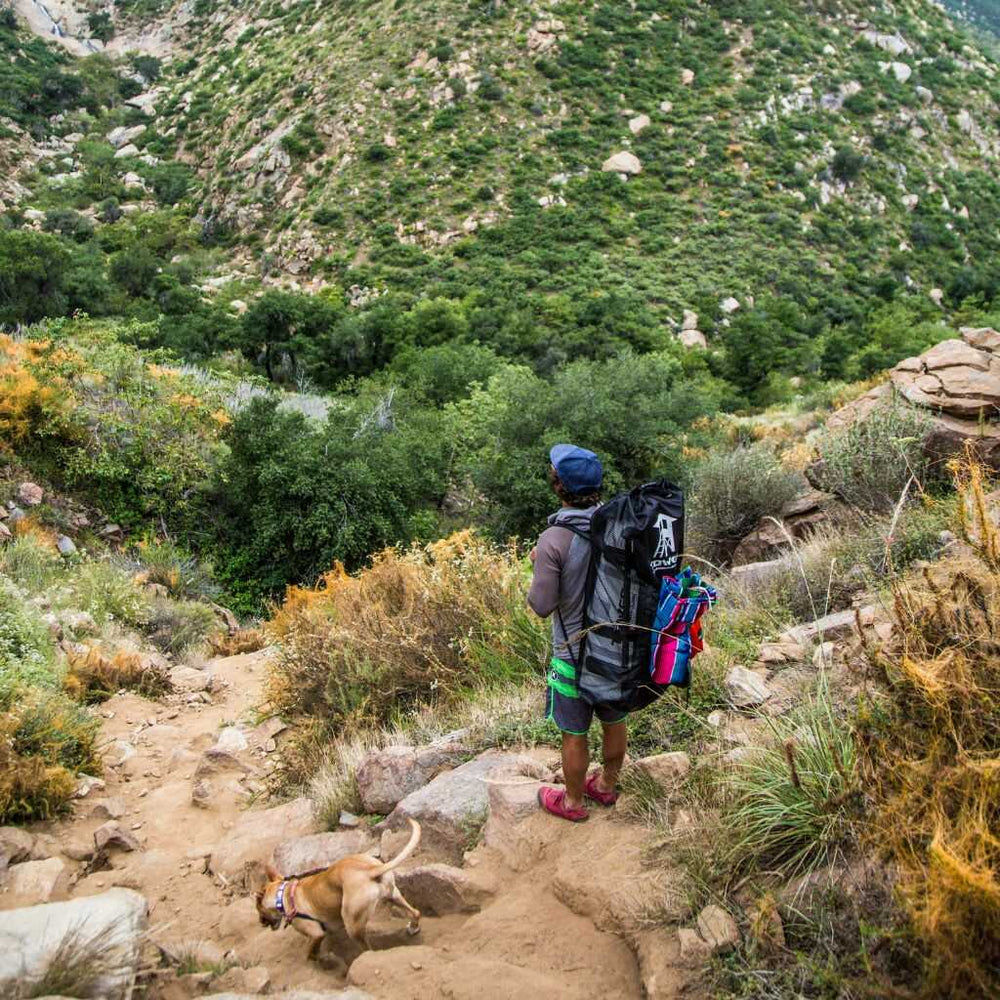 Man standing on a trail in grassy hills while wearing a full iSUP backpack from Tower