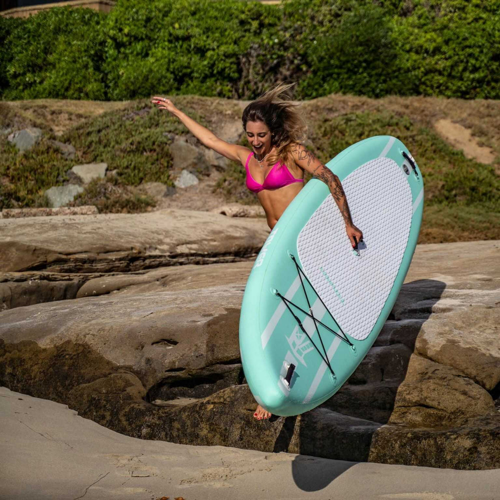 Woman jumping down a ledge while holding a Mermaid paddle board from Tower