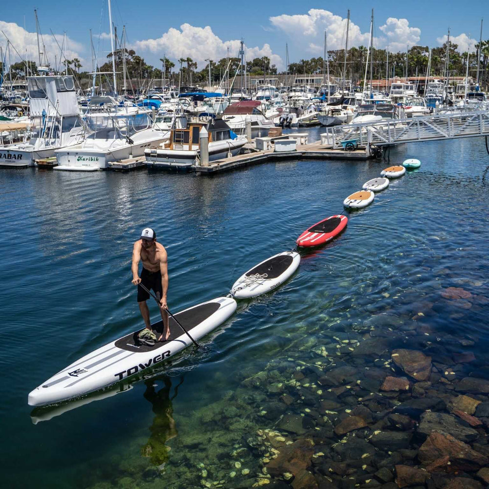 Man paddling a chain of Tower paddle boards through a marina