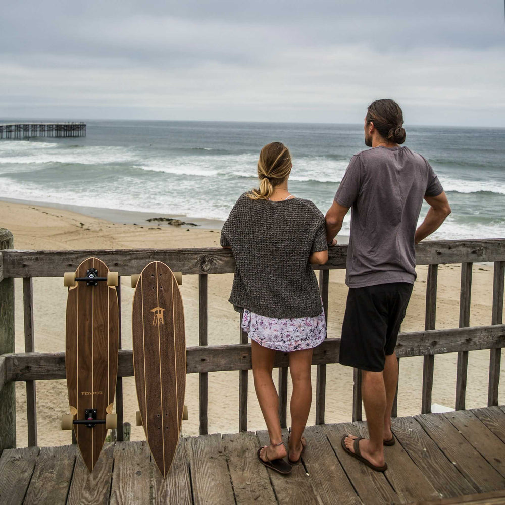 Couple standing together overlooking the ocean with Tower boardwalk cruiser skateboards hanging next to them. 