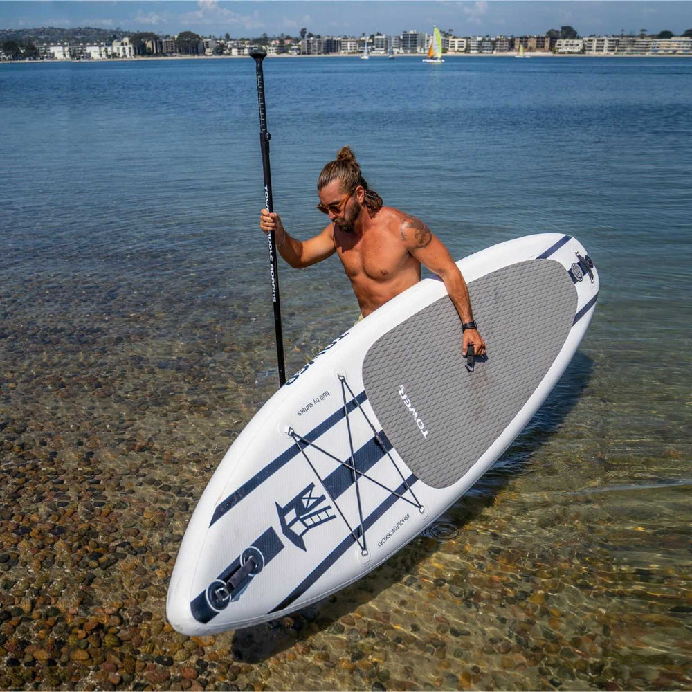 Man getting out of the water with a Tower paddle board and paddle. 