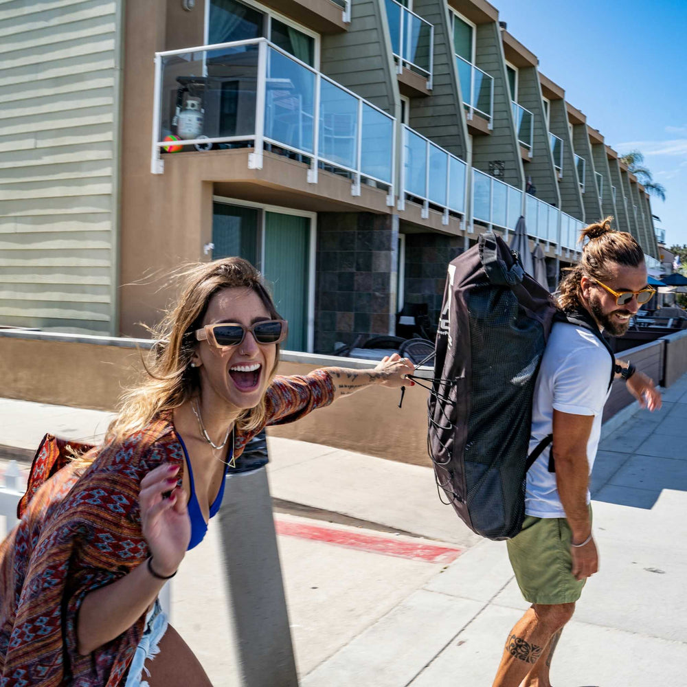 Woman pulling on an iSUP backpack while a man is wearing it. 