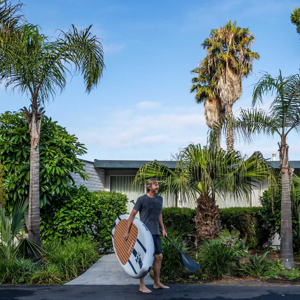 Man carrying a Tower paddle board and paddle