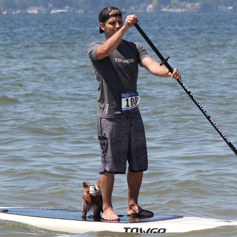 Man paddeling in a Tower paddle Boards shirt with a dog