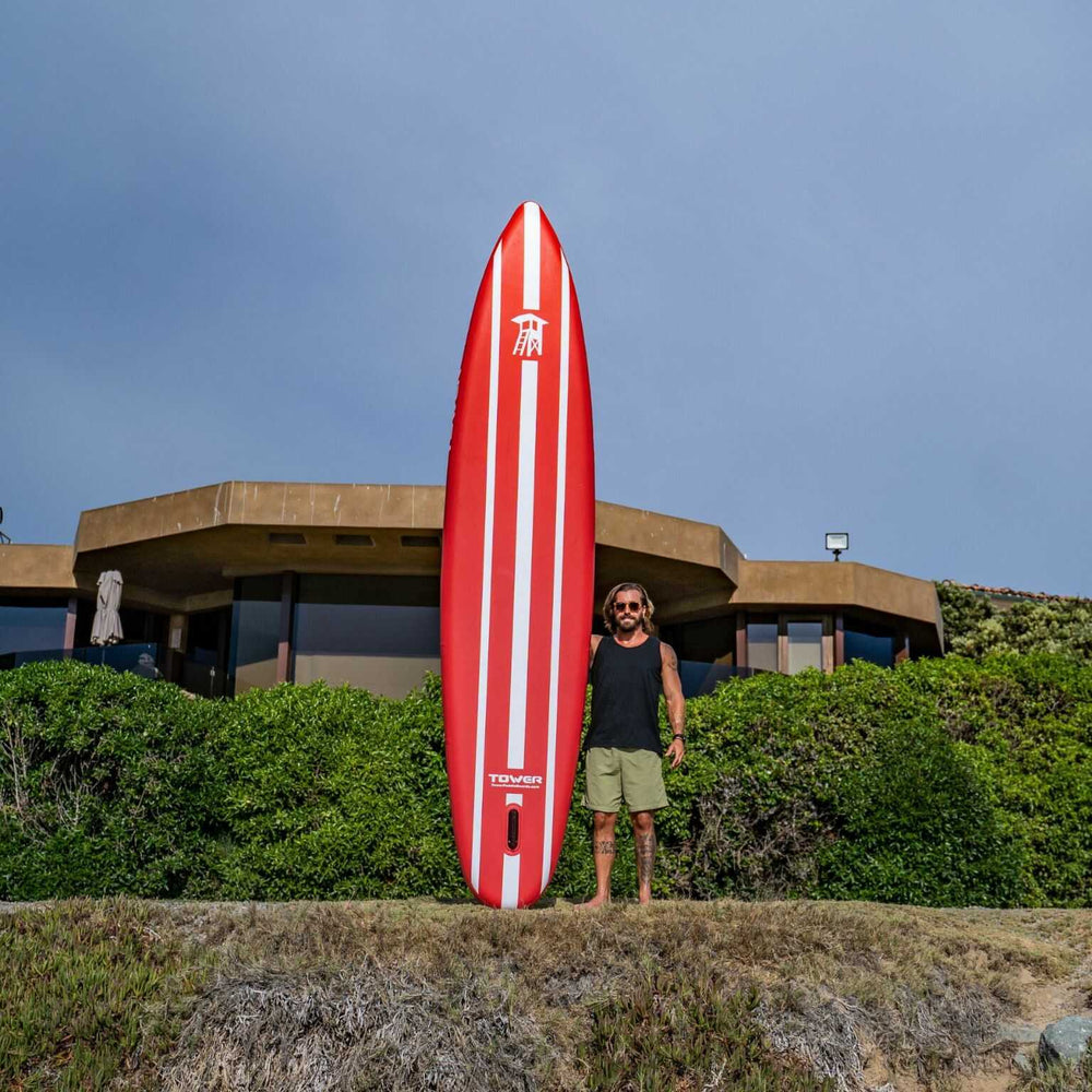 Man standing with Tower iRace paddle board while standing in front of nice house