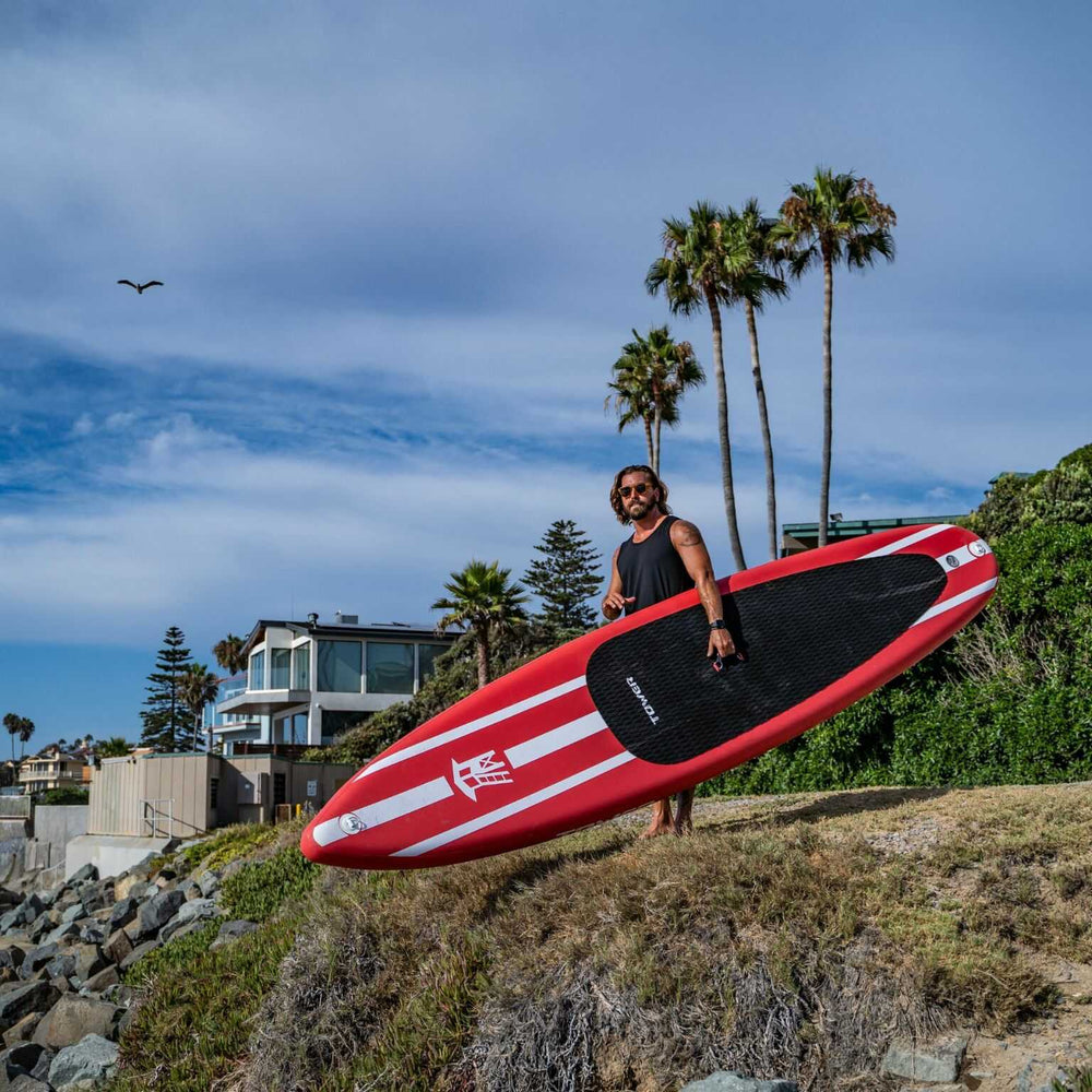 Man carrying iRace paddle board under his arm while standing on a cliff edge