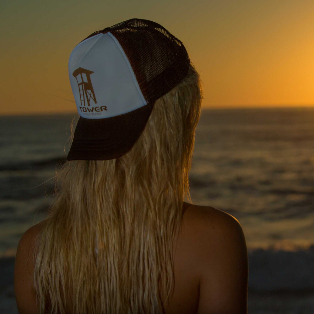 Girl wearing Tower trucker hat backwards looking over the ocean