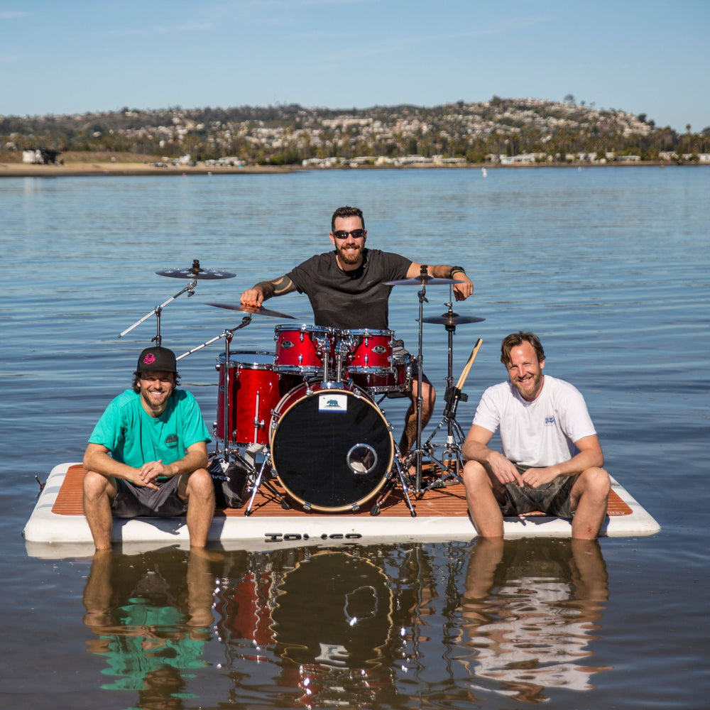 Man with drum set on Tower swim step in the water with 2 guys sitting on the front