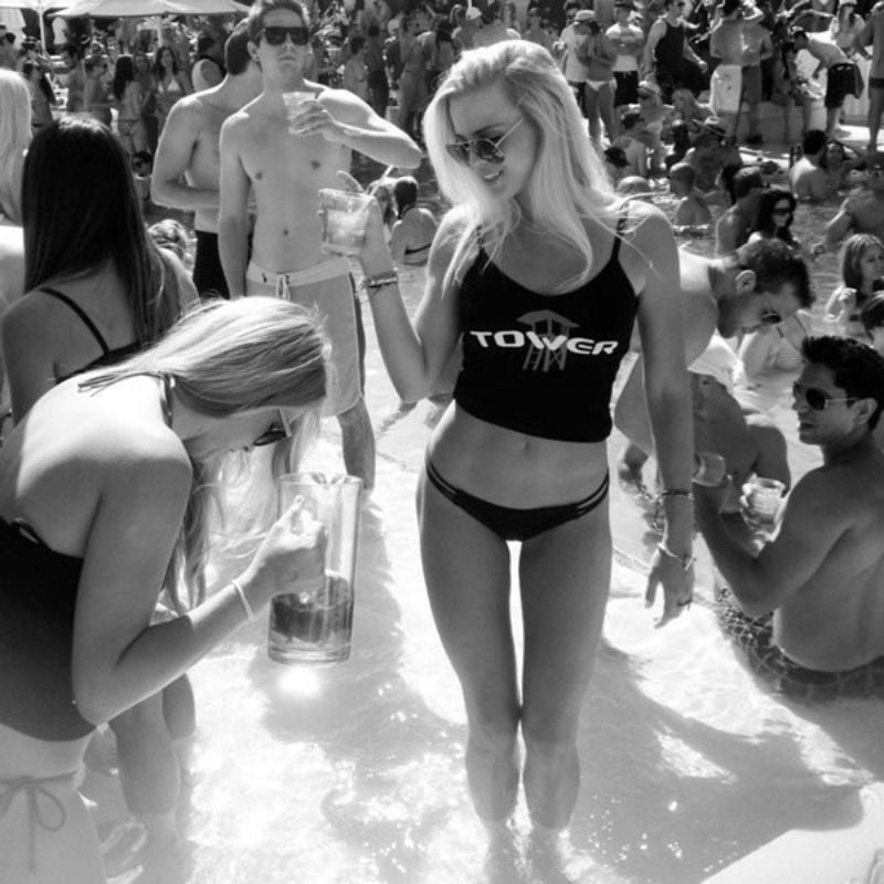 Woman holding a drink in crowd of people wearing a Tower tank top