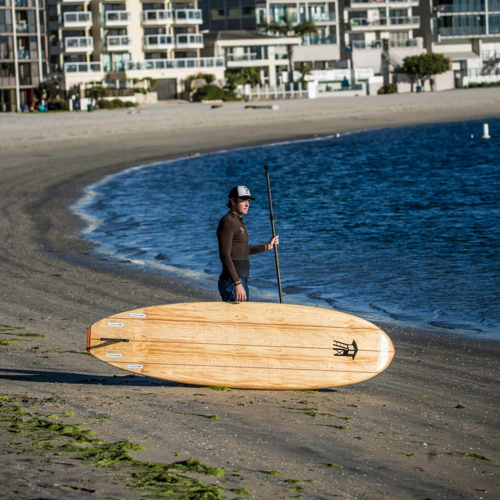 Man standing with a Tower wood paddle board on the shoreline
